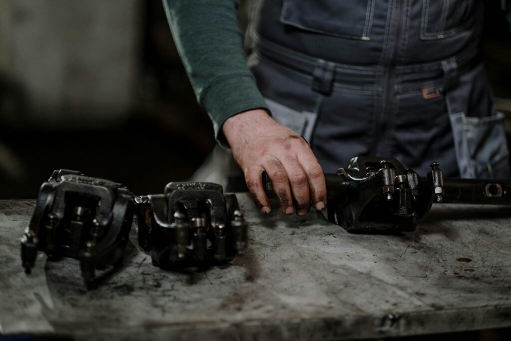 pexels-photo-7568431-7568431 Mechanic in workshop handling greasy metal parts on workbench, depicting repair process.